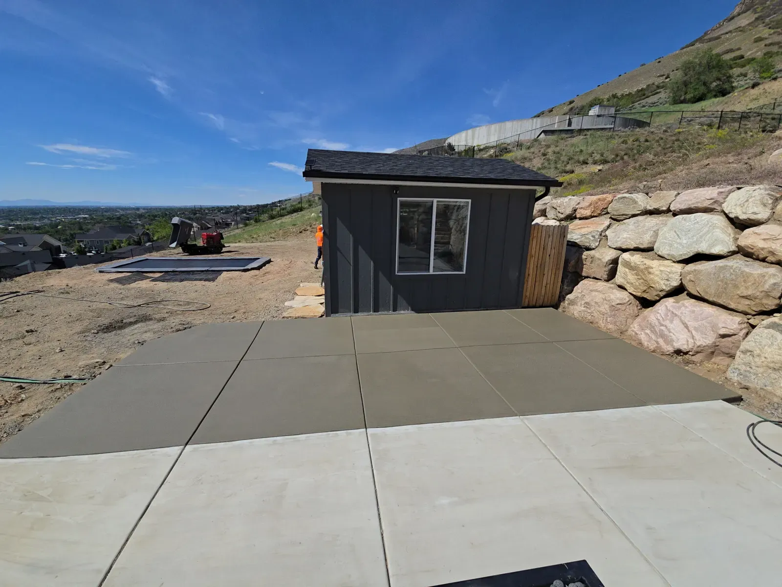 Concrete pad beside a boulder retaining wall and shed in Farmington