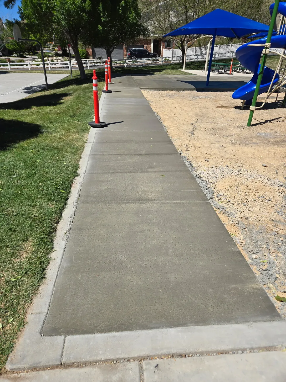 New broom-finish sidewalk with control joints beside a Farmington playground