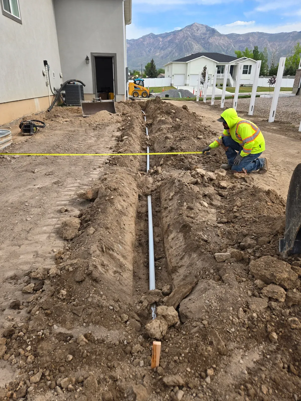 Crew measuring a trench with irrigation pipe laid for a Harrisville sprinkler install