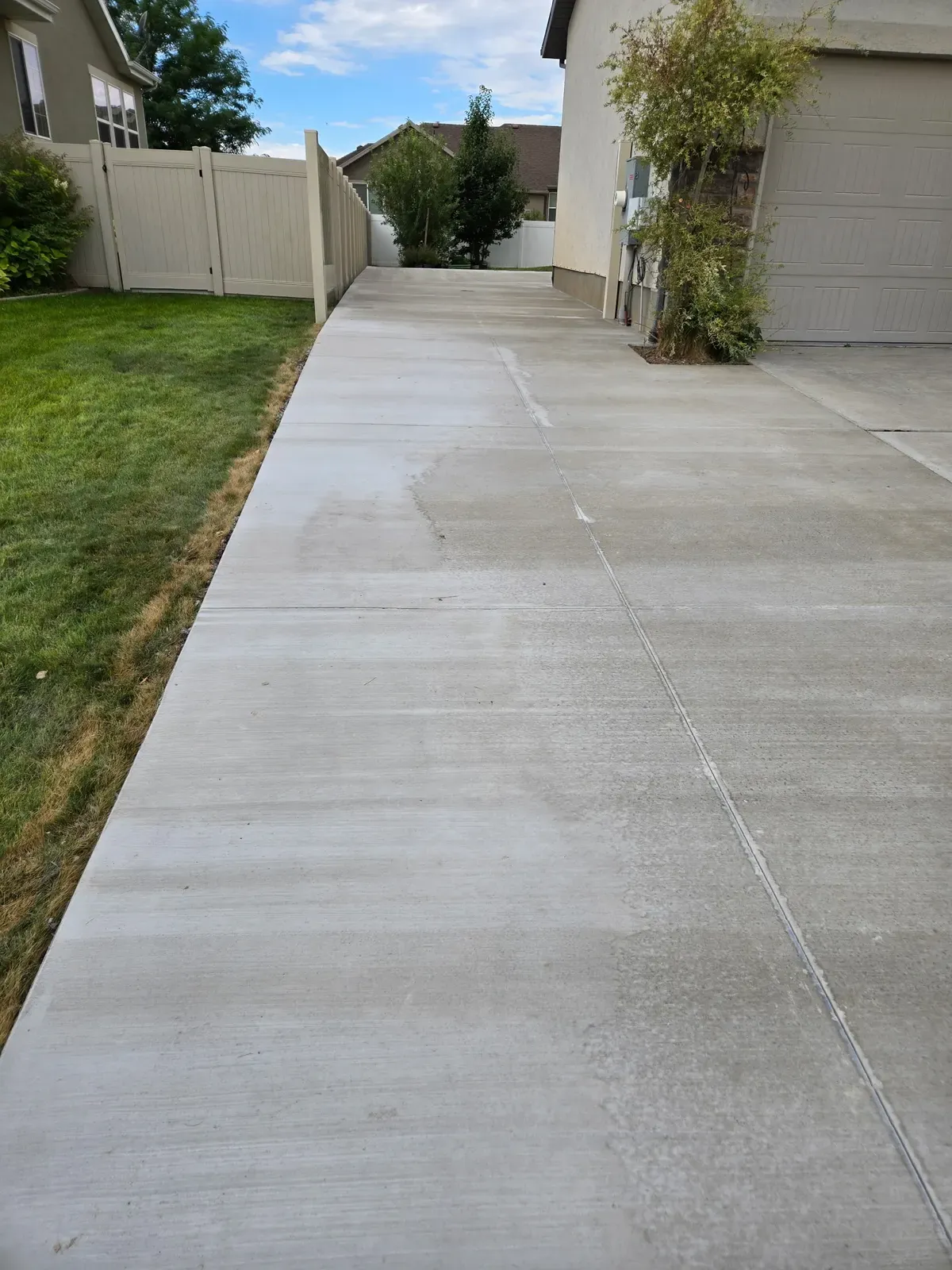 Long broom-finish concrete side walkway between a Roy house and fence
