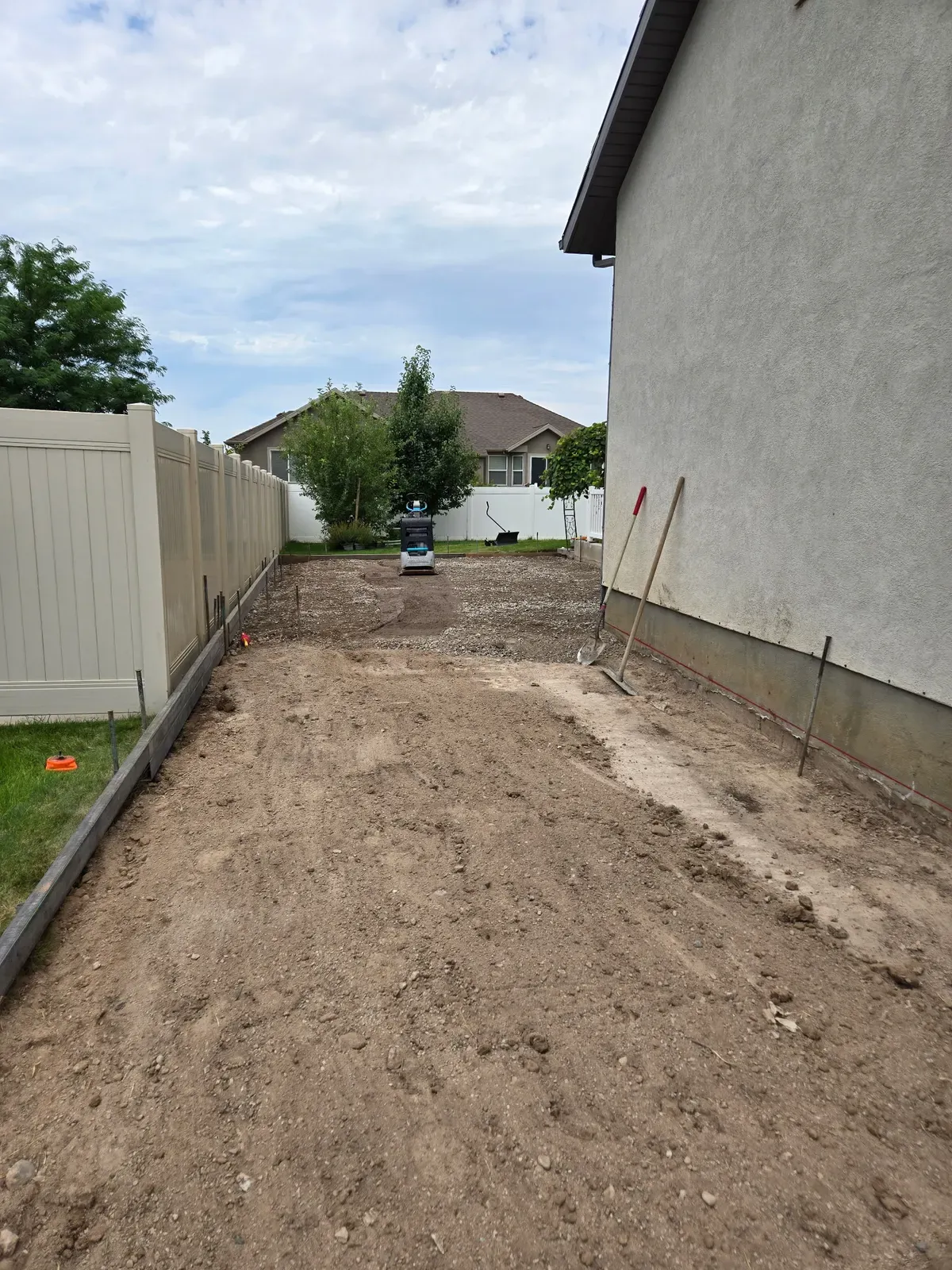 Gravel base, forms, and a plate compactor ready for a Roy side walkway